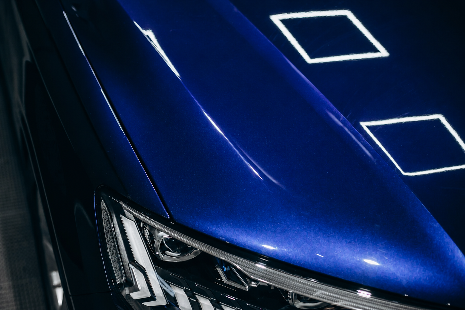 Detalle del acabado azul metalizado y del faro de un vehículo.